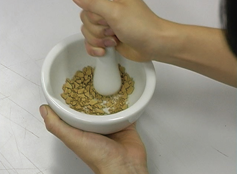 Place some mud pigment in a mortar and grind it with a pestle.